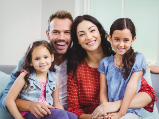 Portrait of parents sitting with daughters on sofa at home